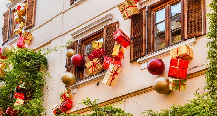 Façade de bâtiment décorée de boîtes-cadeaux suspendues et d'ornements géants entre des fenêtres à volets.