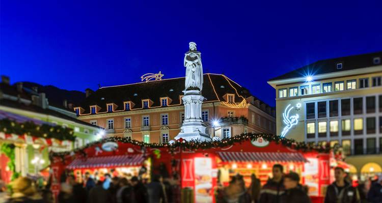 Statue de Walther von der Vogelweide dominant les foules floues sur le marché de Noël du soir lumineux.