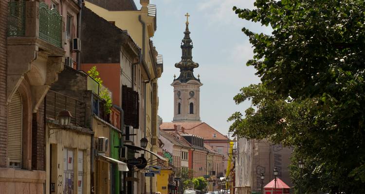Charmante Europese straat met pastelkleurige gebouwen die uitkomt op een hoge sierlijke kerktoren met een kruis erop.