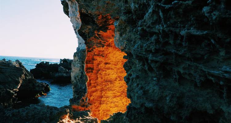 Cueva marina de piedra caliza iluminada por el sol que brilla en naranja donde se encuentra con el océano azul en la costa de Australia Occidental.