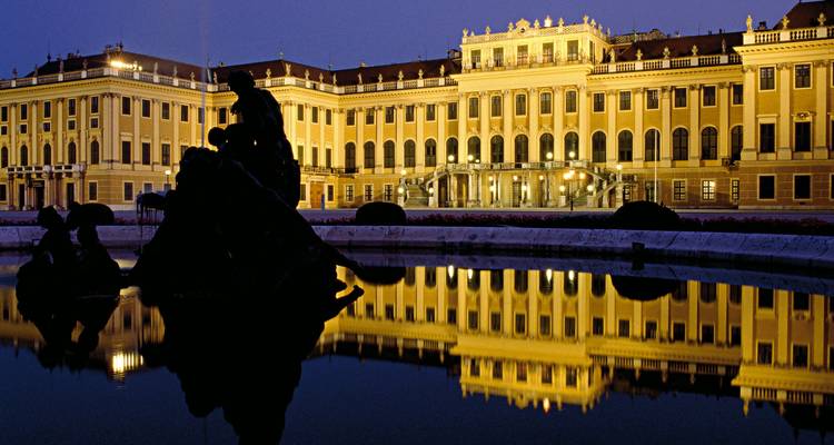 Nighttime reflection of illuminated Schönbrunn Palace on a still ornamental pool.