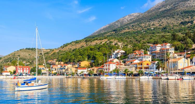 Encantador pueblito costero con casitas coloridas y veleros reflejados en las tranquilas aguas del Mediterráneo bajo un cielo azul.