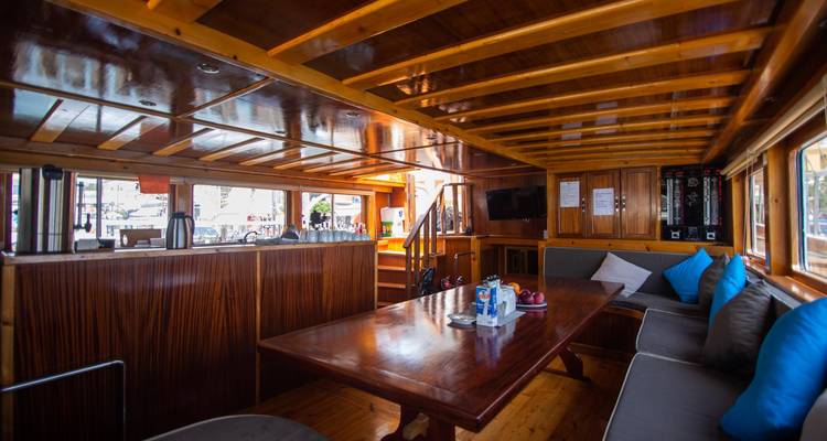 Acogedora sala interior de madera de un barco tradicional con asientos, mesa y zona de bar.