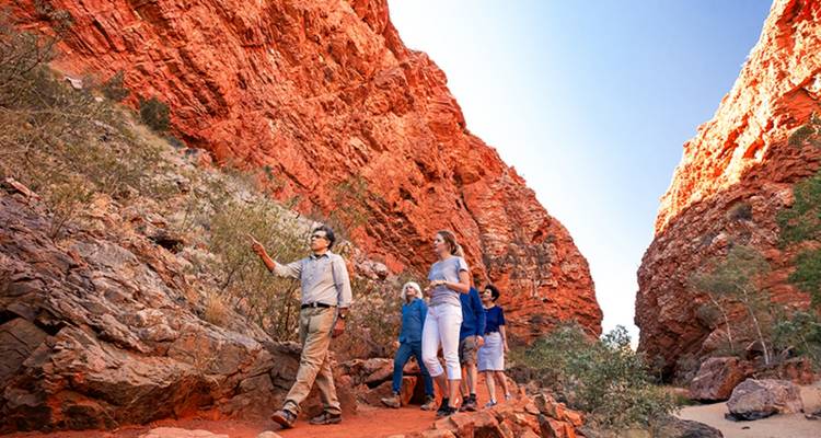 Ein Führer führt eine kleine Gruppe durch die hohen roten Sandsteinwände einer Outback-Schlucht.