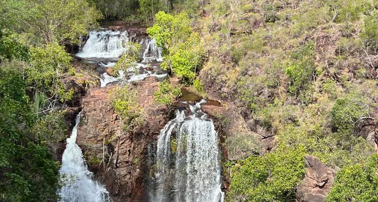 Gestufte Kaskaden stürzen durch grünes Buschland in Felsbecken im Litchfield National Park.