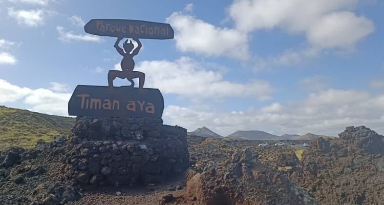 Panneau de diable en métal emblématique marquant l'entrée du parc national de Timanfaya situé dans un paysage de lave et sous un ciel bleu.