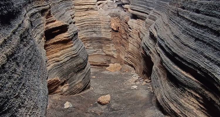Canyon volcanique en couches avec parois texturées aux teintes de gris et de brun.