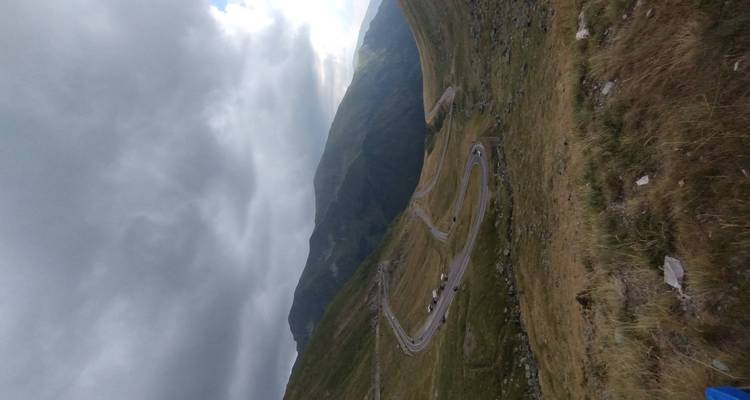 Route de montagne sinueuse serpentant à travers une vallée alpine verdoyante sous des nuages menaçants.
