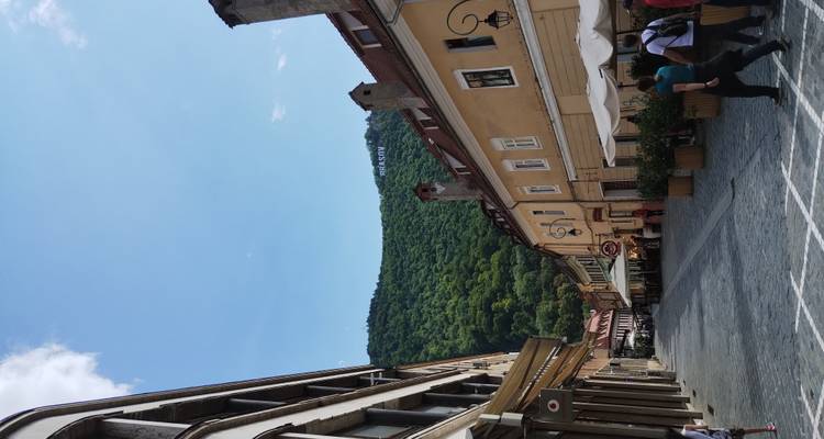 Rue piétonne bordée de cafés et de maisons aux couleurs pastel menant vers une colline verdoyante avec l'enseigne BRASOV.