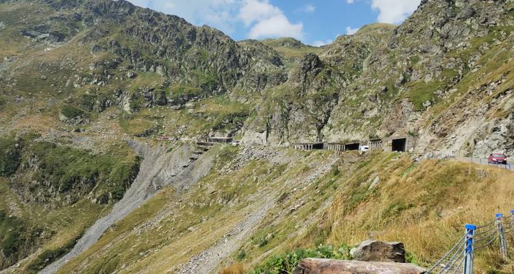 Pente des Montagnes Rocheuses avec des tunnels routiers accrochés aux falaises et des voitures lointaines sous un ciel lumineux.