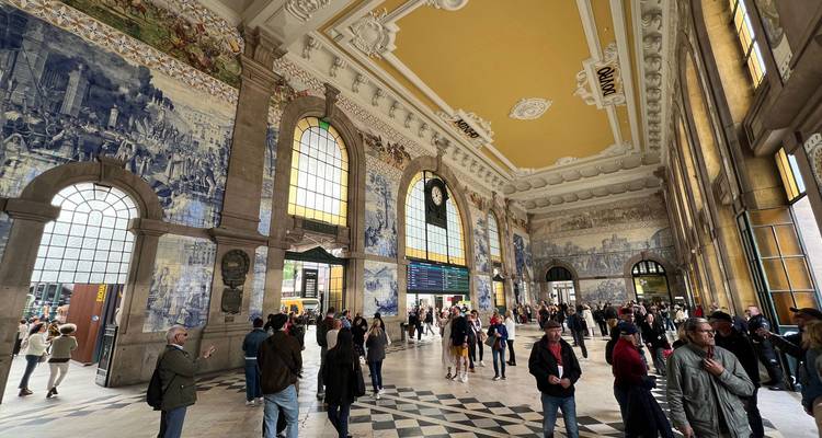 Hall animé d'une gare ferroviaire historique revêtue de mosaïques murales bleues et de grandes fenêtres en arche.