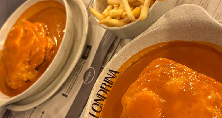 Plat traditionnel portugais de francesinha recouvert d'une sauce riche, servi avec des frites.