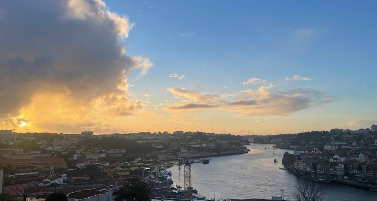 Coucher de soleil doré sur le fleuve Douro avec paysage urbain et nuages illuminés.
