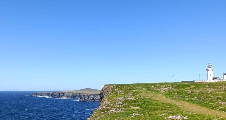 Phare blanc se dressant sur la falaise herbeuse surplombant l'océan Atlantique bleu profond.