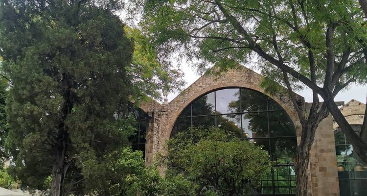 Historische Steinbogenstruktur, umgeben von belaubten Bäumen in einer Gartenanlage