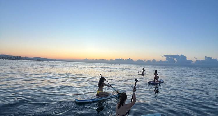 Junge Reisende beim Stand-up-Paddleboarding auf ruhigen Meereswassern während eines farbenfrohen Sonnenuntergangs.