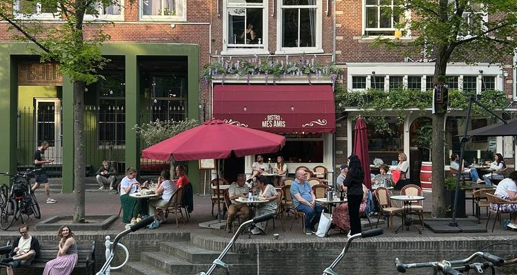 Canal-side bistro with outdoor seating and red umbrellas where guests enjoy drinks and meals.