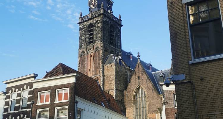 Tall dark church tower rising above traditional Dutch houses under a clear morning sky.