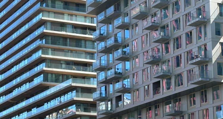 Close-up view of two modern high-rise apartment blocks with glass balconies reflecting the blue sky