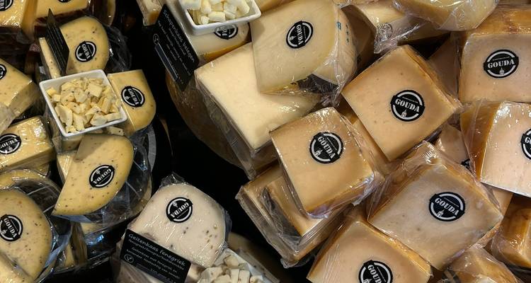 Stacks of wrapped Gouda cheese wheels and samples on display at a market
