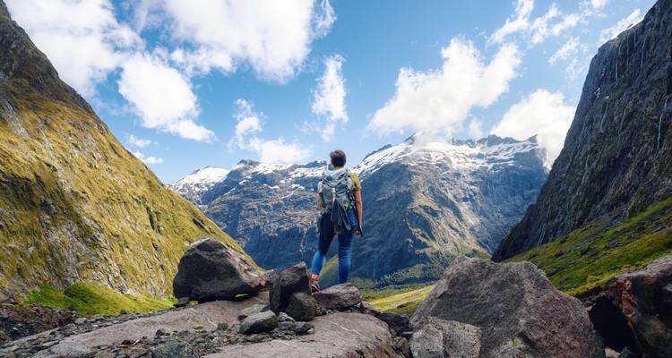 Routard debout parmi les rochers admirant les pics enneigés du Fiordland