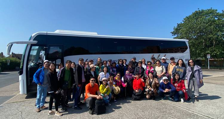 Eine große Reisegruppe posiert vor einem modernen weißen Reisebus unter einem klaren blauen Himmel.