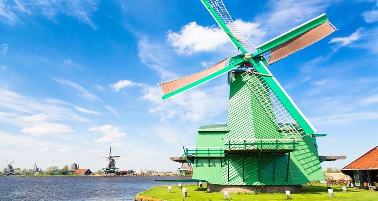 Leuchtend grüne traditionelle Windmühle neben einem ruhigen Fluss unter einem leuchtend blauen Himmel in Zaanse Schans.