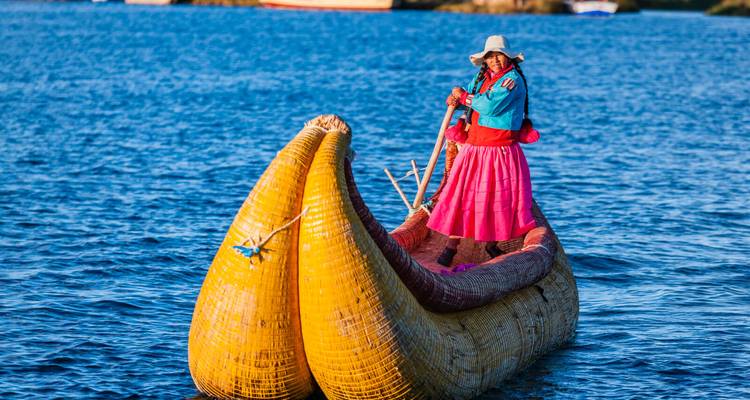 Frau in traditioneller Kleidung paddelt Schilfboot auf dem tiefblauen Lago Titicaca