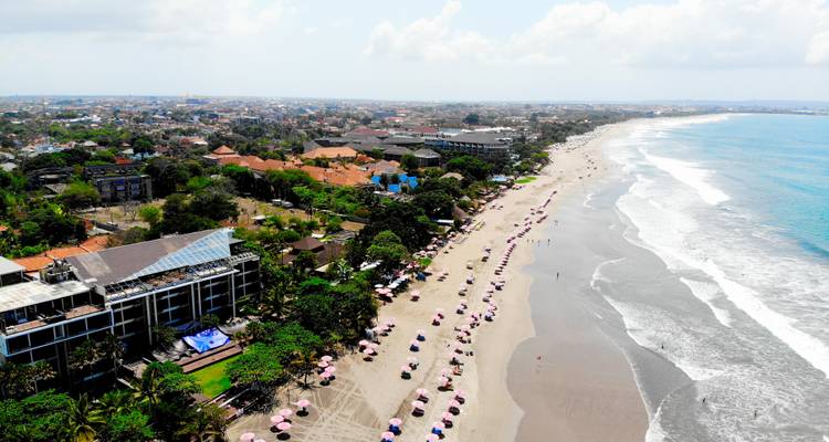 Vue aérienne d'une longue plage de sable fin parsemée de parasols roses et de vagues douces le long de la côte de Bali.