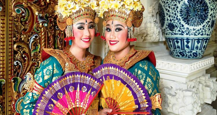 Des artistes balinais souriants vêtus de costumes cérémoniels ornés et de coiffures florales tenant des éventails colorés.
