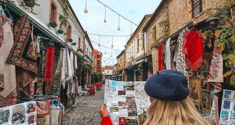 Vista trasera de una mujer con mapa caminando por una colorida calle de mercado de artesanías de los Balcanes