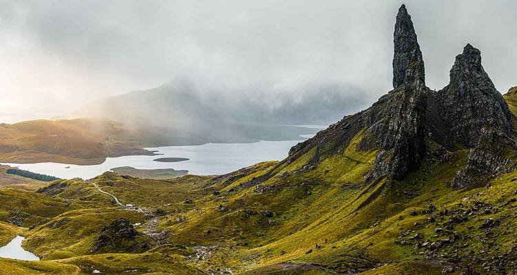 Vista brumosa del pico Old Man of Storr elevándose sobre las laderas verdes y los lagos distantes en la Isla de Skye.