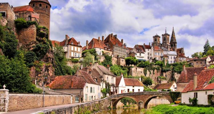 Pittoresque ville médiévale avec des maisons aux toits rouges et des clochers d'églises s'élevant au-dessus d'un pont de pierre et d'une rivière.