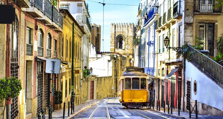Classic yellow tram climbing a narrow, colourful Lisbon street toward the castle walls