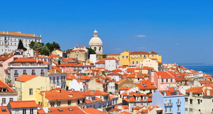 Bright view over Lisbon’s Alfama district with white dome and red rooftops against blue sky