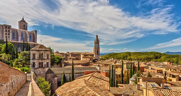 Steinkirchen und mittelalterliche Dächer krönen die goldene Stadtsilhouette von Girona unter einem leuchtend blauen Himmel.