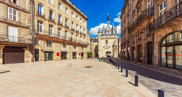Ruhiger Steinplatz, der zum kunstvollen Tor Porte Cailhau unter strahlend blauem Himmel in Bordeaux führt