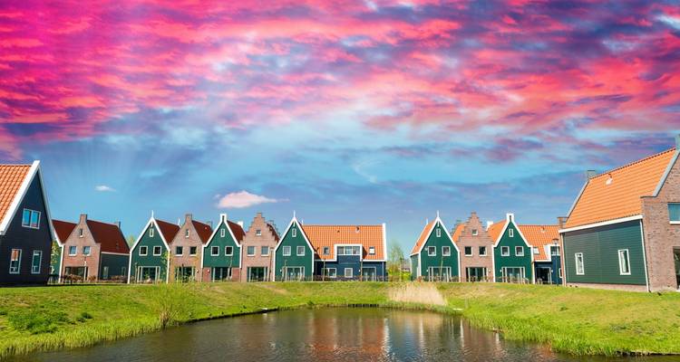 Fila de casas holandesas tradicionales verdes y de ladrillo reflejadas en un estanque tranquilo bajo un cielo de atardecer rosa vivido.
