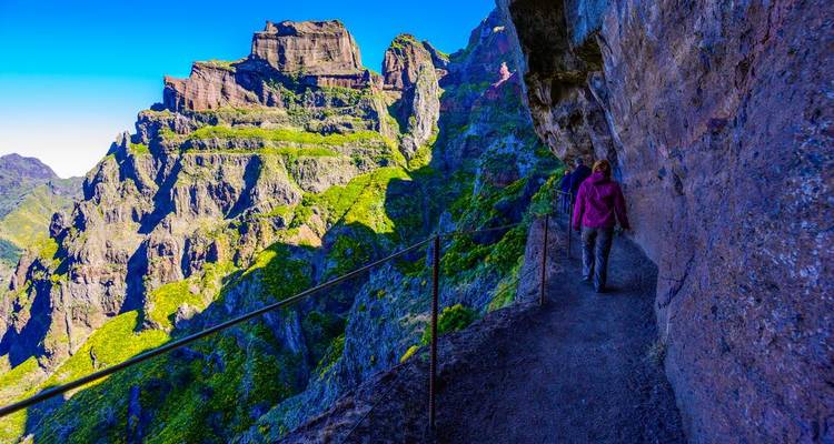 Vivid cliff trail with lone hiker against bright green peaks and deep blue sky on Madeira.
