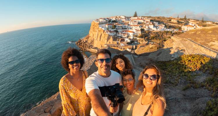 Lächelnde Gruppen-Selfie auf einer Klippe mit Blick auf weiße Küstenortgebäude in der goldenen Stunde in Portugal