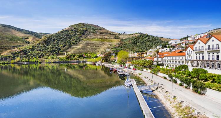 Klare Aussicht entlang des Ufers des Douro mit terrassenförmig angelegten Weinbergen, die die Hügel hinaufsteigen, und hellem blauen Himmel