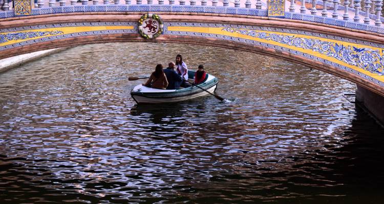 Petite barque avec des amis pagayant sous le pont en céramique coloré du canal de la Plaza de España