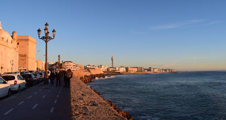 Longue promenade côtière à Cadix à la lumière dorée avec des habitants marchant à côté des remparts de la ville