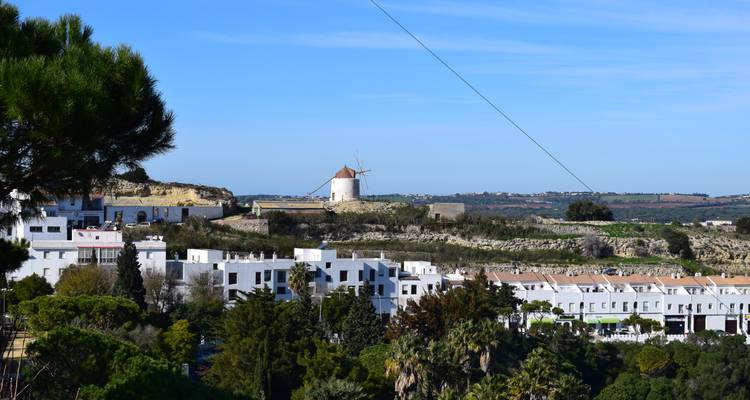 Vue campagnarde mettant en vedette un moulin à vent blanc solitaire au sommet d'une colline avec des maisons blanches dispersées en contrebas