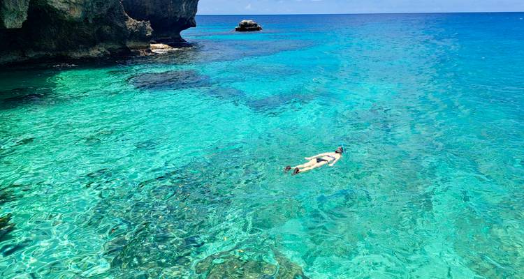 Un plongeur en apnée glisse dans une eau turquoise cristalline à côté de falaises côtières spectaculaires.