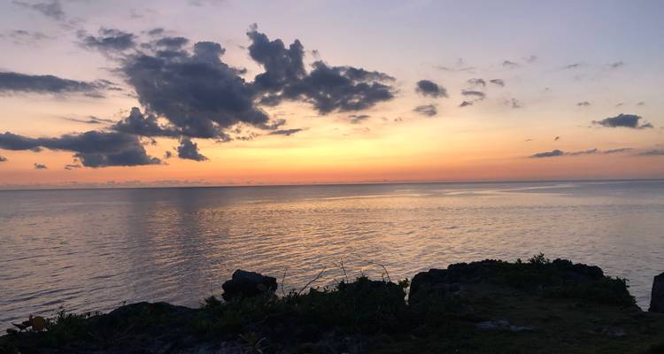 L'horizon de l'océan calme s'illumine de teintes chaudes d'orange et de violet lors d'un coucher de soleil tranquille.