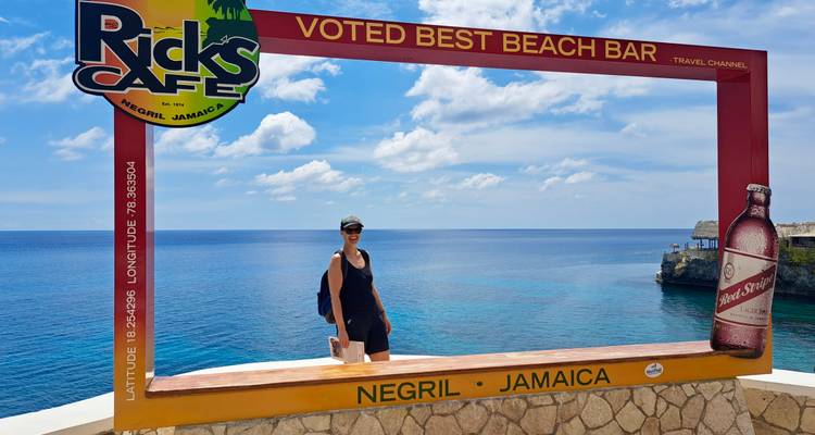 Un voyageur pose à l'intérieur d'un cadre photo du Rick's Café Negril avec vue sur la mer des Caraïbes d'un bleu éclatant et les falaises.