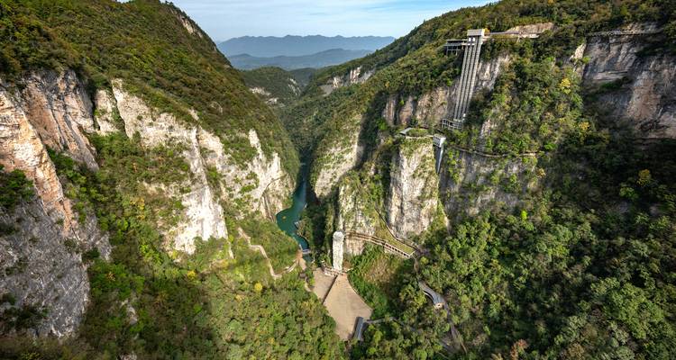 Luftaufnahme der dramatischen Zhangjiajie-Schlucht mit Glassbrücke, die sich zwischen steilen bewaldeten Felswänden erstreckt.