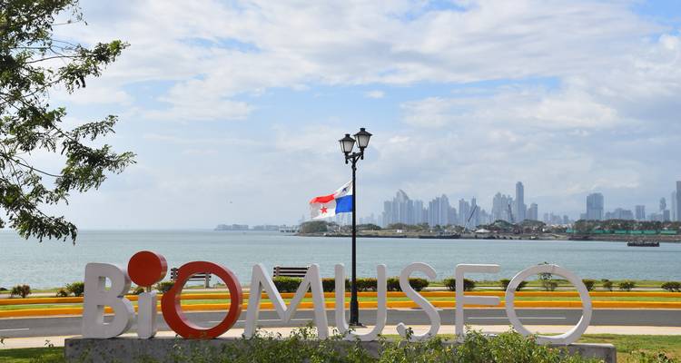 Buitenbord van het BioMuseo met Panamese vlag en moderne skyline van Panama City aan de overkant van de baai.