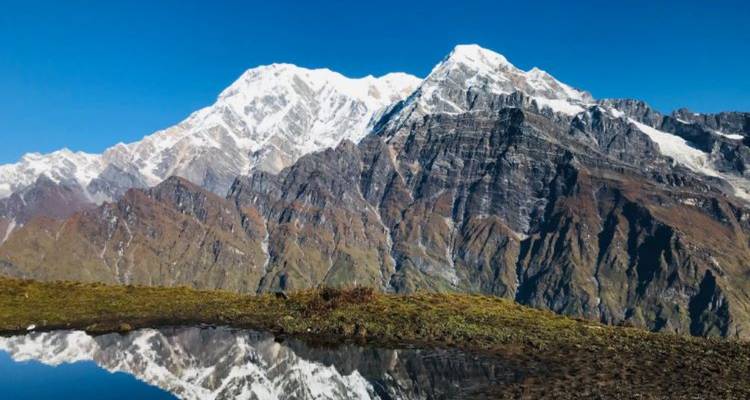 Des pics enneigés et dentelés de l'Himalaya se reflétant dans un étang alpin tranquille sous un ciel dégagé